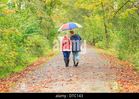 Jeune couple se promener le long de l'country lane avec parapluie coloré Banque D'Images