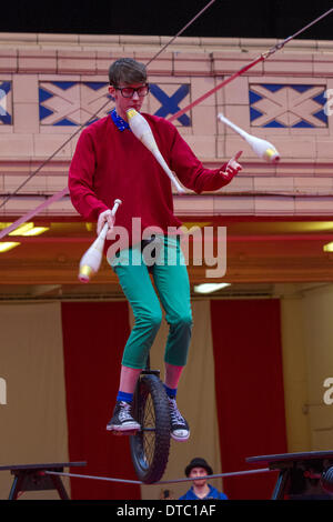 Man Riding Unicycle Along High Wire Juggling à Blackpool, Lancashire, Royaume-Uni 14 février 2014. NoFit State Circus est une société de cirque contemporaine qui se déroule au festival annuel de cirque, de magie et de nouvelle variété de Blackpool. Le festival de magie de dix jours qui est Showzam voit les célèbres monuments de Blackpool envahi par les marcheurs, les conjurés et les artistes de rue les plus serrés. Le festival se déroule chaque année à Blackpool, un festival extraordinaire et unique qui comprend un certain nombre d'artistes de haut niveau, des artistes de rue, du cirque, de la magie et de la nouvelle variété et jamais vu des actes présentés dans toute la ville. Banque D'Images