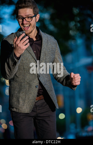 Jeune homme excité looking at mobile phone, Toronto, Ontario, Canada Banque D'Images