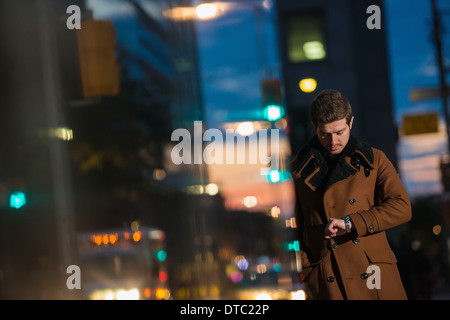 Jeune homme attendant sur street looking at watch, Toronto, Ontario, Canada Banque D'Images