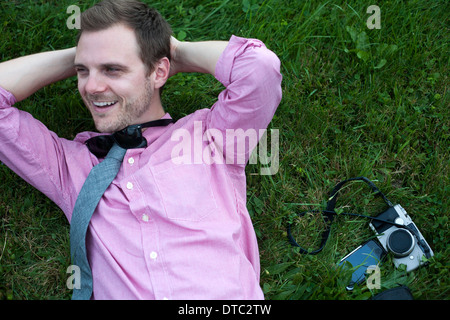 Mid adult man avec caméra et smartphone relaxing on grass Banque D'Images