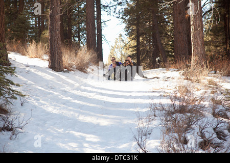 Garçon et les jeunes adultes de la luge dans la forêt enneigée Banque D'Images