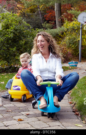 Jeune mère et son riding on toy cars in garden Banque D'Images