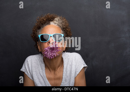 Studio portrait of senior woman with flower in her mouth Banque D'Images