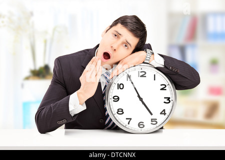 Sleepy man posant sa tête sur une grande horloge murale, à l'intérieur Banque D'Images