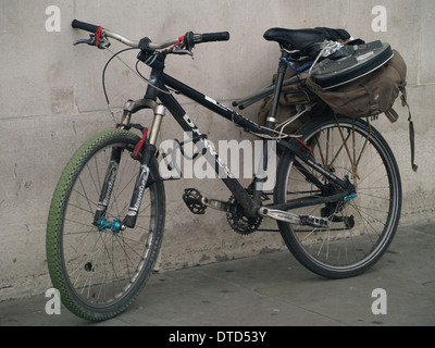 Vélo avec sacoches gauche contre un mur de béton en ville Banque D'Images