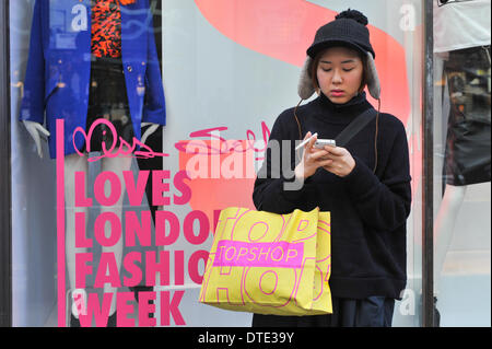 Oxford Street, Londres, Royaume-Uni. 16 février 2014. Une fille utilise un iPhone en face de la Miss Selfridge fenêtre sur Oxford Street. Banque D'Images