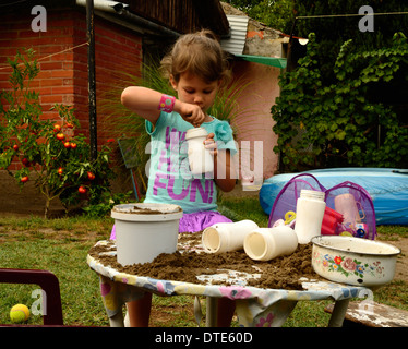 Petite fille jouant avec du sable sur la table de jardin Banque D'Images