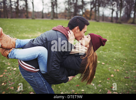 Beau jeune homme portant sa jolie petite amie et s'embrasser. Mixed Race couple dans l'amour en plein air dans le parc. Banque D'Images