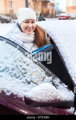 Femme souriante avec balai à neige et voiture enneigée Banque D'Images