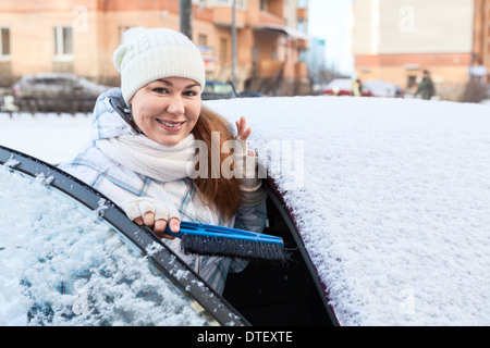 Jolie femme avec balai à neige et voiture enneigée Banque D'Images