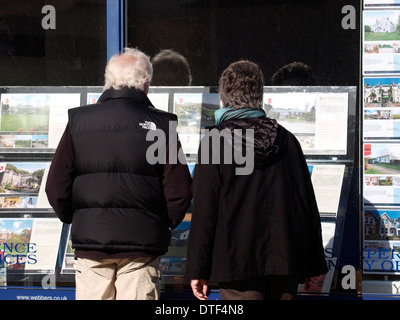 Vieux couple à la recherche sur des maisons dans une fenêtre d'agents immobiliers, Bude, Cornwall, UK Banque D'Images