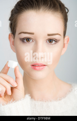 Un joli teenage girl holding un cube de sucre près de sa tête. Banque D'Images