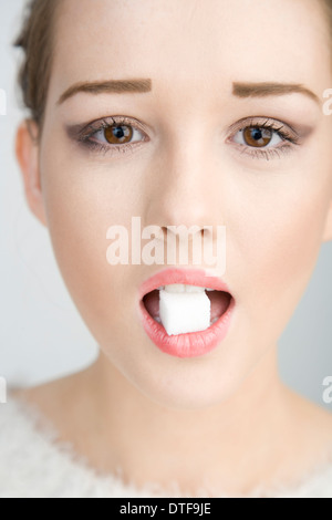 Un joli teenage girl holding un cube de sucre dans sa bouche. Banque D'Images