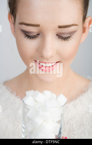 Une jeune femme à la recherche vers le bas dans un verre rempli de cubes de sucre. Banque D'Images