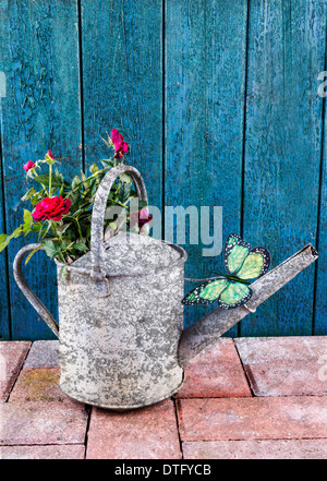 Vintage arrosoir avec roses sur un patio contre une vieille porte Banque D'Images