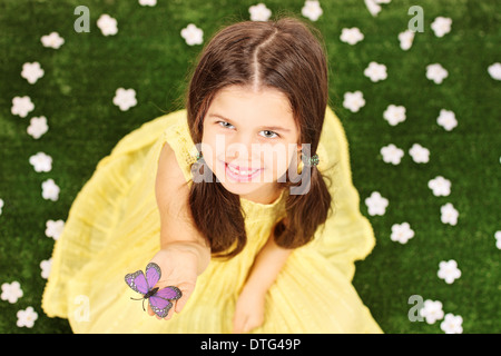 Little girl holding un papillon dans un champ plein de fleurs Banque D'Images