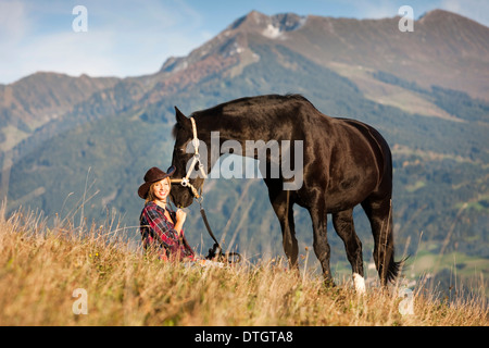 Une jeune femme avec un cheval hanovrien noir sur une prairie de montagne en automne, Tyrol du Nord, Autriche Banque D'Images