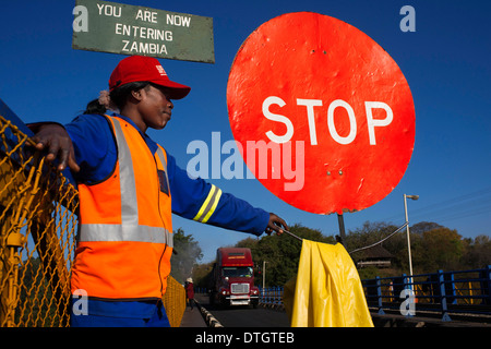 Une femme contrôle le trafic entre la Zambie et le Zimbabwe. Un panneau d'arrêt indique que nous entrons dans la Zambie. Banque D'Images