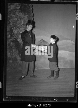 Cette photographie capture un homme et un garçon en costumes de théâtre sur scène, accompagnés de cages à oiseaux et d'accessoires de scène. L'image, qui fait partie de la collection de l'Université de Miami, reflète l'importance des productions théâtrales et de l'éducation des femmes dans les premières représentations. Banque D'Images
