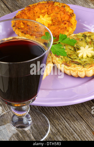 Assortiment de mini quiches végétariennes, servis sur une plaque rose et un verre de vin rouge sur un fond de bois Banque D'Images