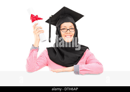 Étudiant islamique féminine avec mortier et veil holding diploma derrière panneau vierge Banque D'Images