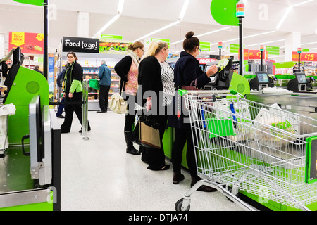 Les clients faisant la queue pour payer à un self service jusqu'à un supermarché Asda. Banque D'Images