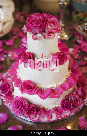 Un gâteau de mariage à trois niveaux couverts en glaçage blanc et décoré avec des pétales de rose en Angleterre Banque D'Images