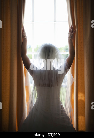 Une femme debout à une fenêtre qui donnait dans une robe de mariée avec voile Banque D'Images