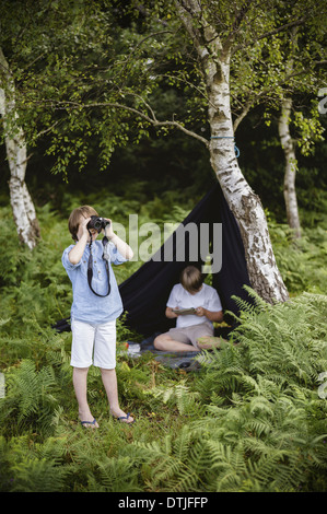 Deux garçons en camping dans une nouvelle forêt assis sous un abri de toile noire un garçon binoculars Hampshire Angleterre Banque D'Images