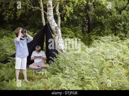 Deux garçons en camping dans une nouvelle forêt assis sous un abri de toile noire un garçon binoculars Hampshire Angleterre Banque D'Images