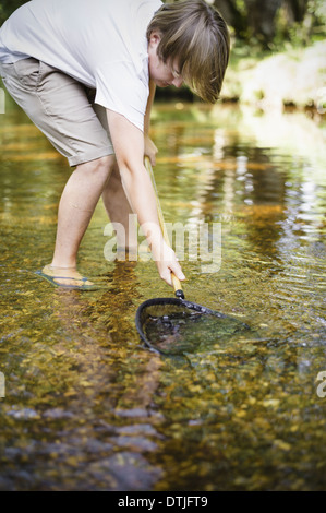 Un petit garçon dans l'eau peu profonde en se penchant et en utilisant un petit filet de pêche Hampshire Angleterre Banque D'Images