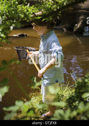 Un jeune garçon tenant un filet de pêche par une rivière peu profonde Camping in the New Forest Hampshire Angleterre Banque D'Images