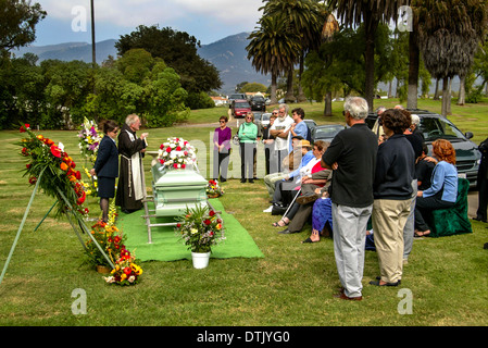 Un prêtre franciscain vêtu lors d'une inhumation dans officie Santa Barbara, CA. Remarque cercueil et fleurs. Banque D'Images