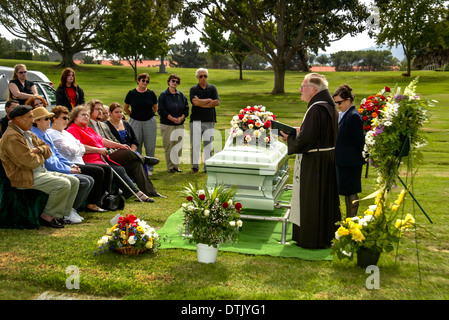 Un prêtre franciscain vêtu lors d'une inhumation dans officie Santa Barbara, CA. Remarque cercueil et fleurs. Banque D'Images