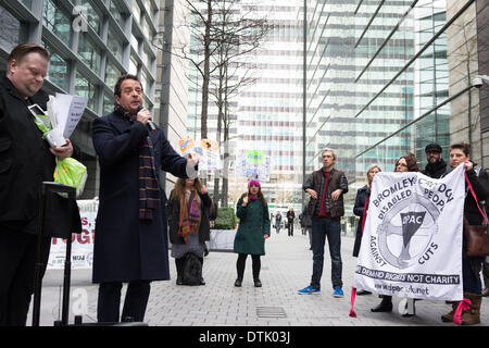 Siège social d'ATOS ORIGIN, London, UK, 19 février 2014. Comédien et activiste Mark Thomas parle à l'extérieur du siège social d'ATOS ORIGIN à Londres pour protester contre la mise en œuvre des travaux d'évaluation des capacités. Mobilité l'interprète et comédien Mat Fraser (cinquième à partir de la droite) à l'écoute de la foule. Les activistes ont appelé à l'abolition de l'évaluation de la capacité de travail et a déclaré qu'un médecin qualifié, idéalement le GP qui voit régulièrement et traite la personne malade ou handicapée en question, est la seule personne capable de décider si une personne est apte au travail. Credit : Patricia Phillips/Alamy Live News Banque D'Images