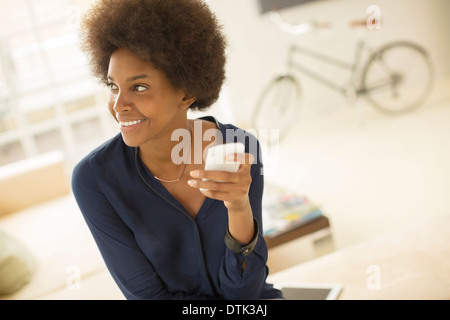 Woman using cell phone in living room Banque D'Images