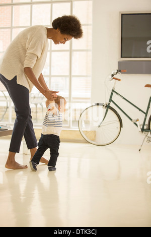 Mother helping baby boy à pied dans la salle de séjour Banque D'Images