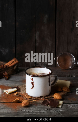 Vintage mug avec la vapeur chaude servi au chocolat avec des morceaux de chocolat blanc et noir et d'amandes sur la vieille table en bois Banque D'Images