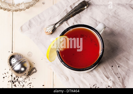 Vue de dessus sur vintage white mug de thé au citron, servi avec du thé et du sucre de la crépine-tongs sur table en bois blanc Banque D'Images