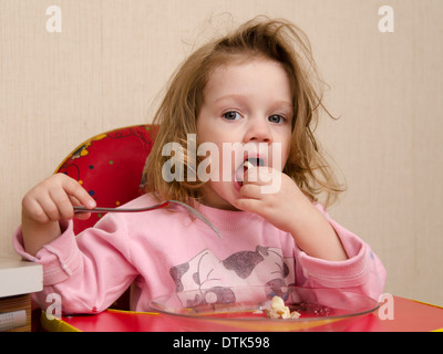 Fillette de deux ans mange assis à table dans la cuisine. Fille mange avec une fourchette. Banque D'Images