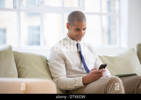 Businessman using cell phone on sofa Banque D'Images