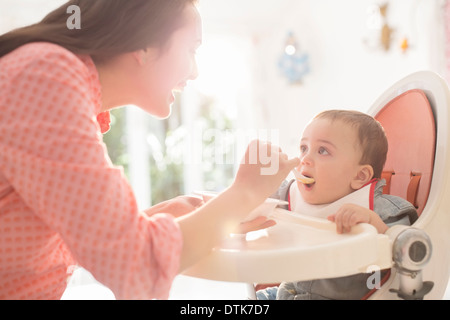 Mère nourrir bébé garçon dans une chaise haute Banque D'Images