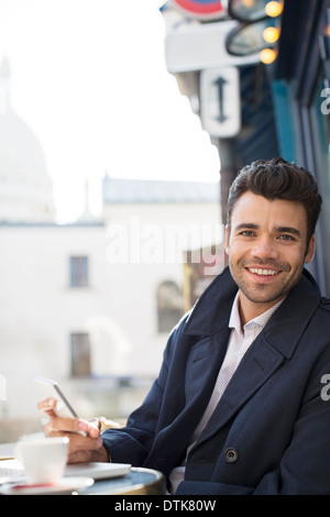 Businessman using cell phone at sidewalk cafe Banque D'Images