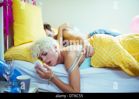 Gueule de woman checking cell phone au lit le matin après une fête Banque D'Images