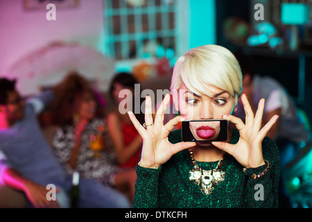 Woman Playing with cell phone in living room at party Banque D'Images