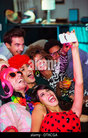 Friends taking self-portrait with camera phone on sofa at party Banque D'Images