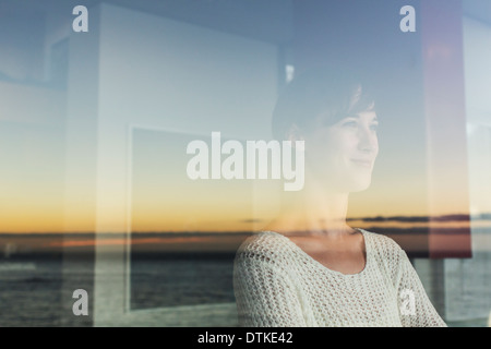 Femme donnant sur le coucher du soleil et l'océan à partir de la fenêtre . Banque D'Images