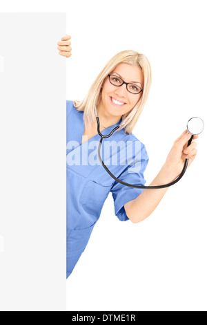 Young female doctor with stethoscope posant derrière panneau vierge Banque D'Images