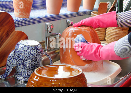 Femme portant des gants de caoutchouc jusqu'à laver les pots à l'évier de cuisine à la maison Banque D'Images